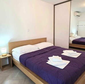 A neatly made bed with a wooden headboard, a bedside table with a lamp, and a large mirror on the wall. - Holiday home with air conditioning and barbecue terrace (Baška)