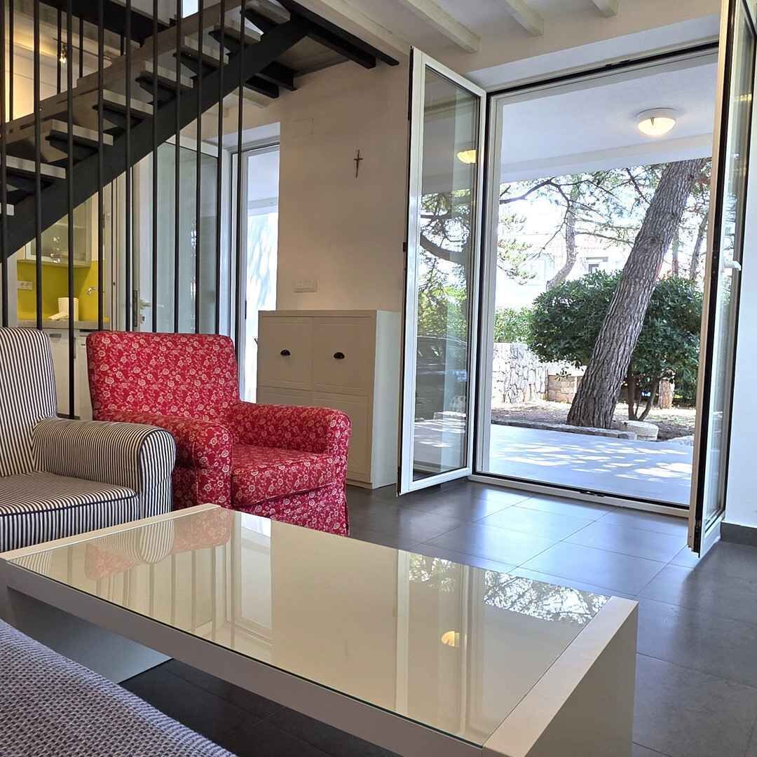 A modern living room with a glass door leading outside, a staircase, and a sofa.