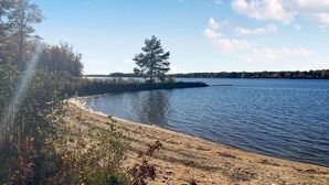 A lakeside view with a sandy beach, a small island with a tree, and a distant shoreline. - Gorgeous home in Bolmsö with lake view (Bolmsö)