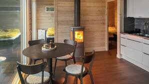 A cozy room with a wood-burning stove, a dining table with chairs, and a kitchen area. - Gorgeous home in Bolmsö with lake view (Bolmsö)