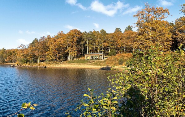 Un chalet au bord du lac, doté d’une terrasse et d’un porche abrité, entouré d’un feuillage automnal et d’arbres.