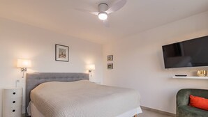 Un dormitorio moderno con una cama grande, un ventilador de techo, un televisor y una silla.