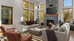 Una sala de estar moderna con chimenea, ventanas grandes y televisor montado.
