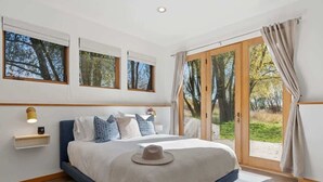 Un dormitorio con cama, mesita de noche, ventana y puerta que da a un balcón.
