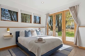 Ein Schlafzimmer mit Bett, Nachttisch, Fenster und einer Tür, die auf einen Balkon führt.