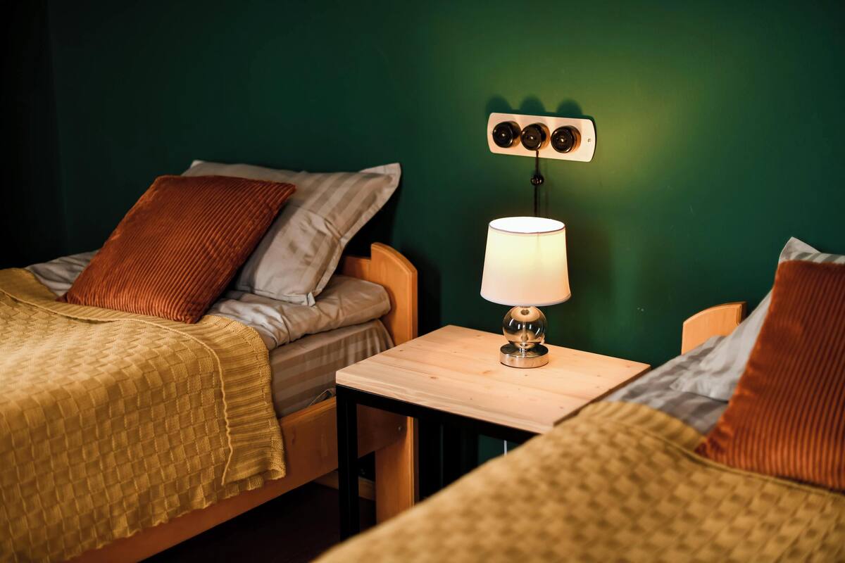 Una stanza con due letti, un tavolo con una lampada e un punto luce a parete.