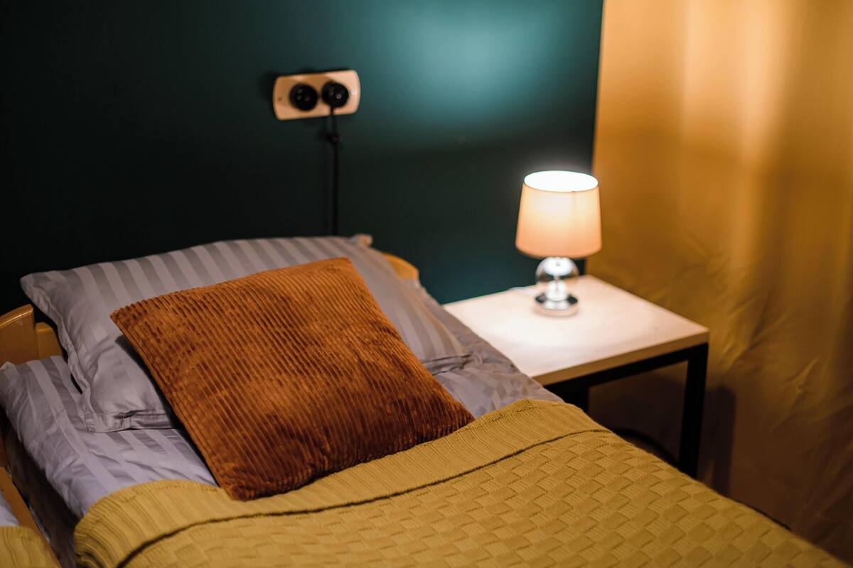 Un letto con un cuscino marrone e una coperta gialla, un comodino con una lampada e una presa elettrica.