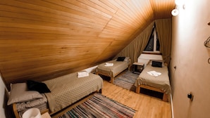 Un dormitorio de buhardilla acogedor con listones de madera en el techo, dos camas individuales, una mesita pequeña y una ventana con cortinas.