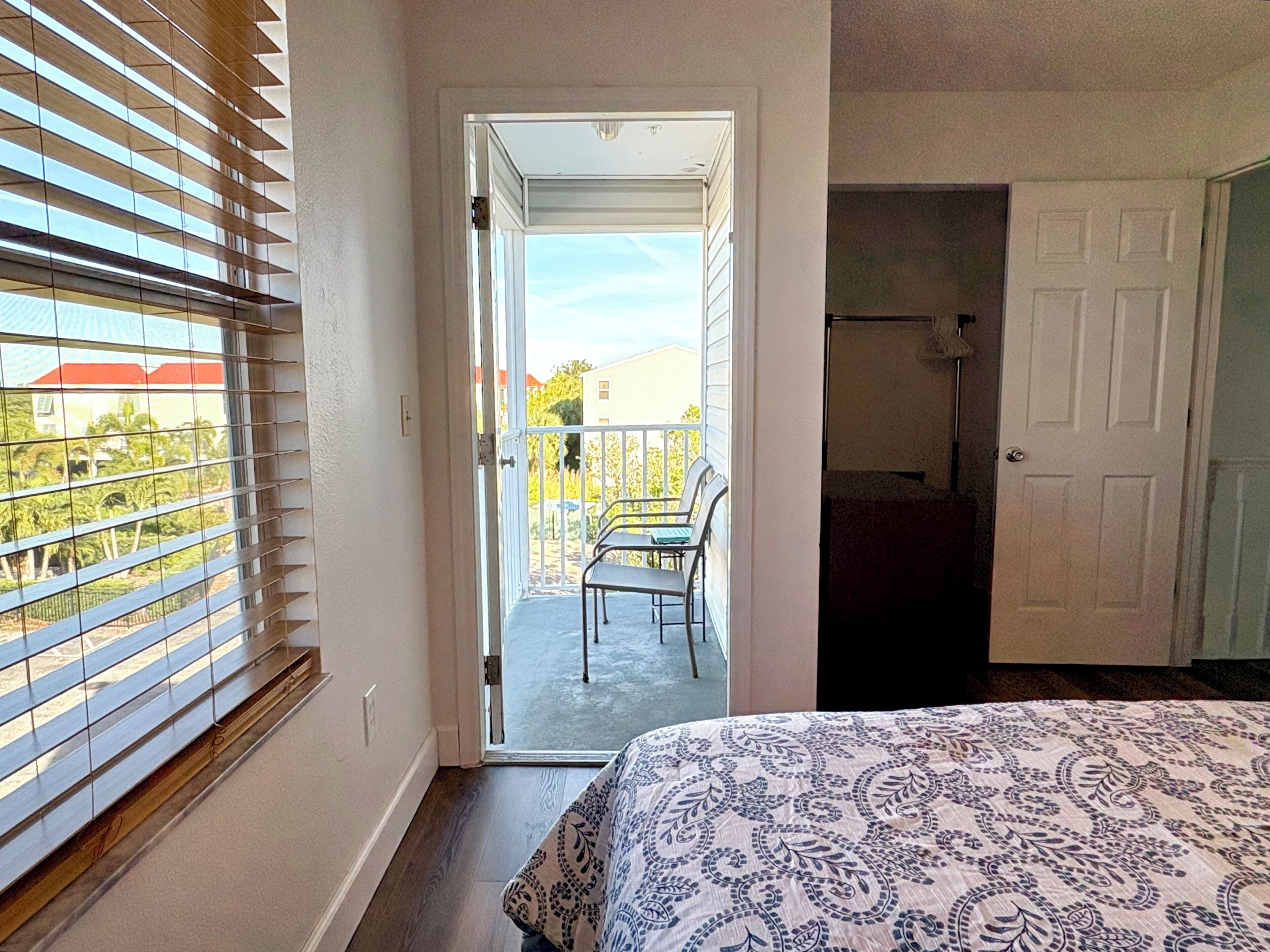 A bedroom with a large window, a balcony with chairs, and a door leading to a bathroom.