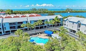 A resort with a swimming pool, multiple-story buildings, and a view of the ocean. - Private balconies, Walk to Holmes Beach, sleeps 8, access to heated pool (Holmes Beach)