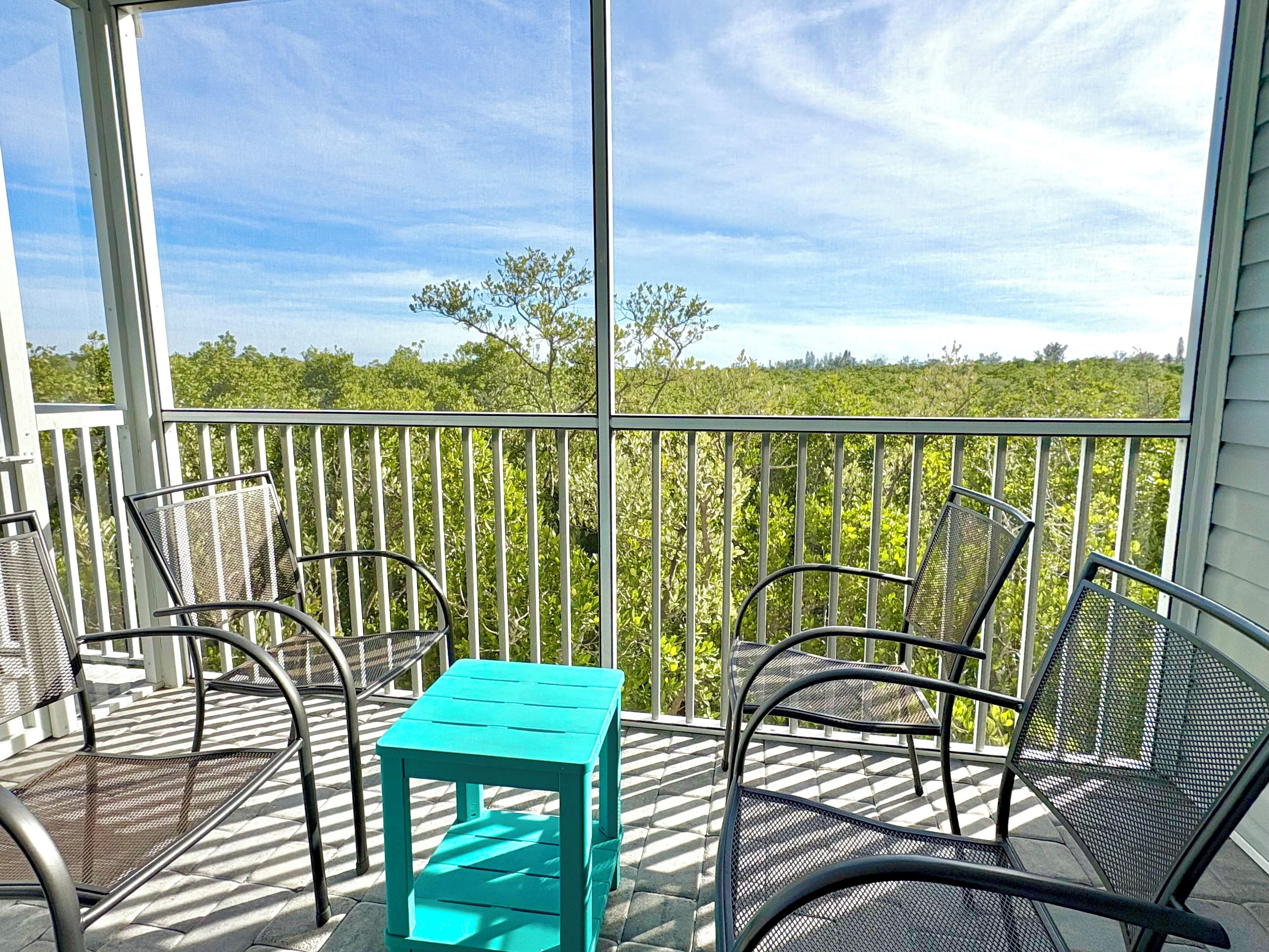 A covered outdoor seating area with metal chairs and a turquoise table, overlooking a lush green landscape.