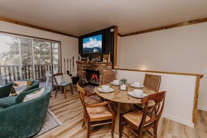 Una sala de estar acogedora con chimenea, un televisor montado encima y una zona de comedor con una mesa y sillas de madera.