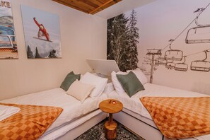 Habitación de hotel con dos camas, una computadora portátil sobre una de ellas y un mural con temática de esquí en la pared.