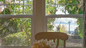 Une pièce avec une chaise en bois et une table, une fenêtre donnant sur un paysage verdoyant et une tour.