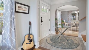 Un couloir avec une guitare en bois, une table en verre avec des pieds en métal et un tapis à motifs.