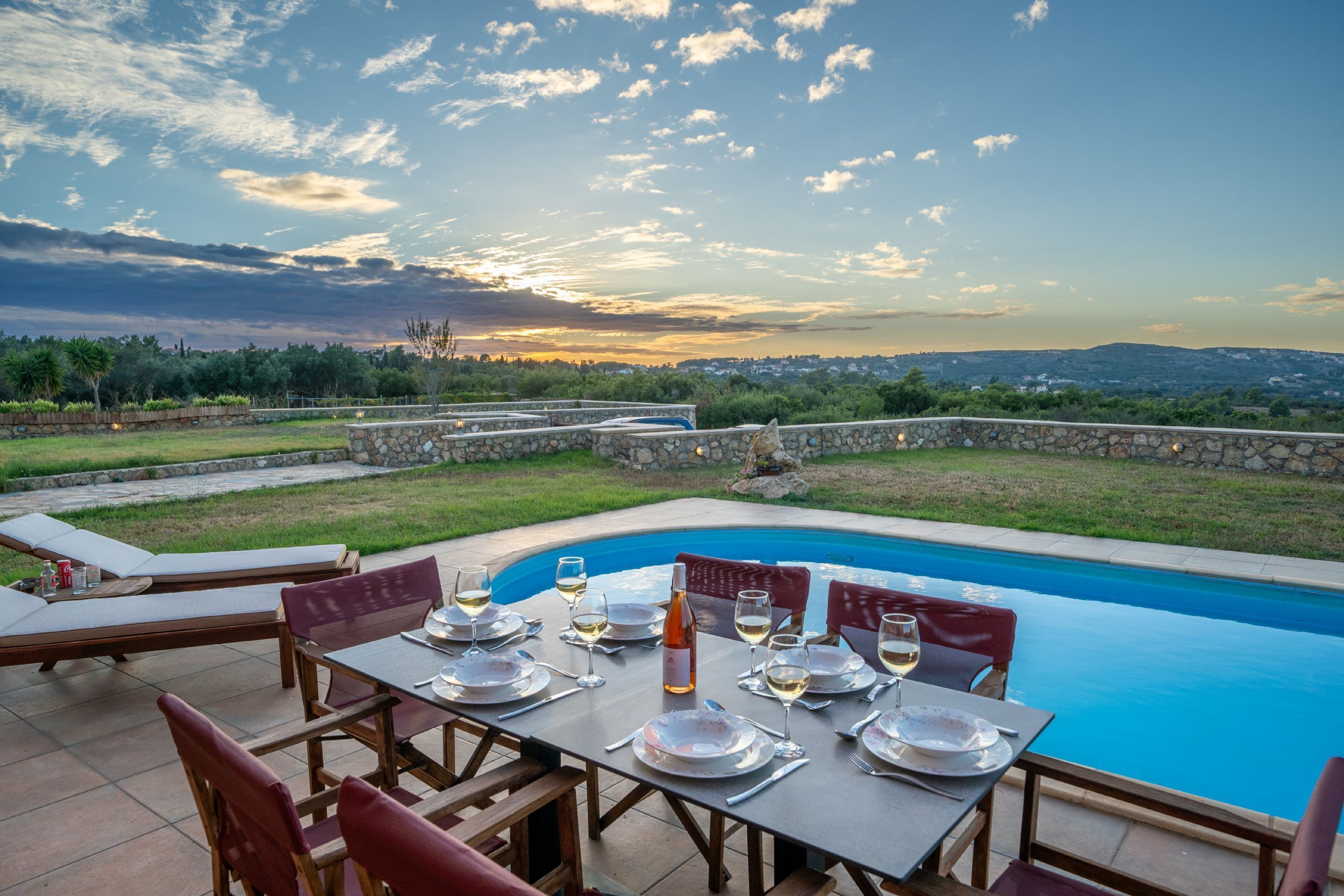 Un área de comedor al aire libre con piscina, muros de piedra y vistas del paisaje.