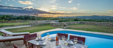 Un área de comedor al aire libre con piscina, muros de piedra y vistas del paisaje.