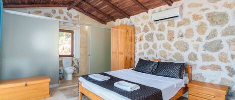 A bedroom with a stone wall, wooden ceiling, a bed with a patterned bedspread, wooden nightstands, and a wooden wardrobe.