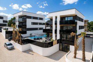 Un hôtel moderne à plusieurs étages, doté d’une piscine, d’un espace extérieur aménagé et de palmiers.