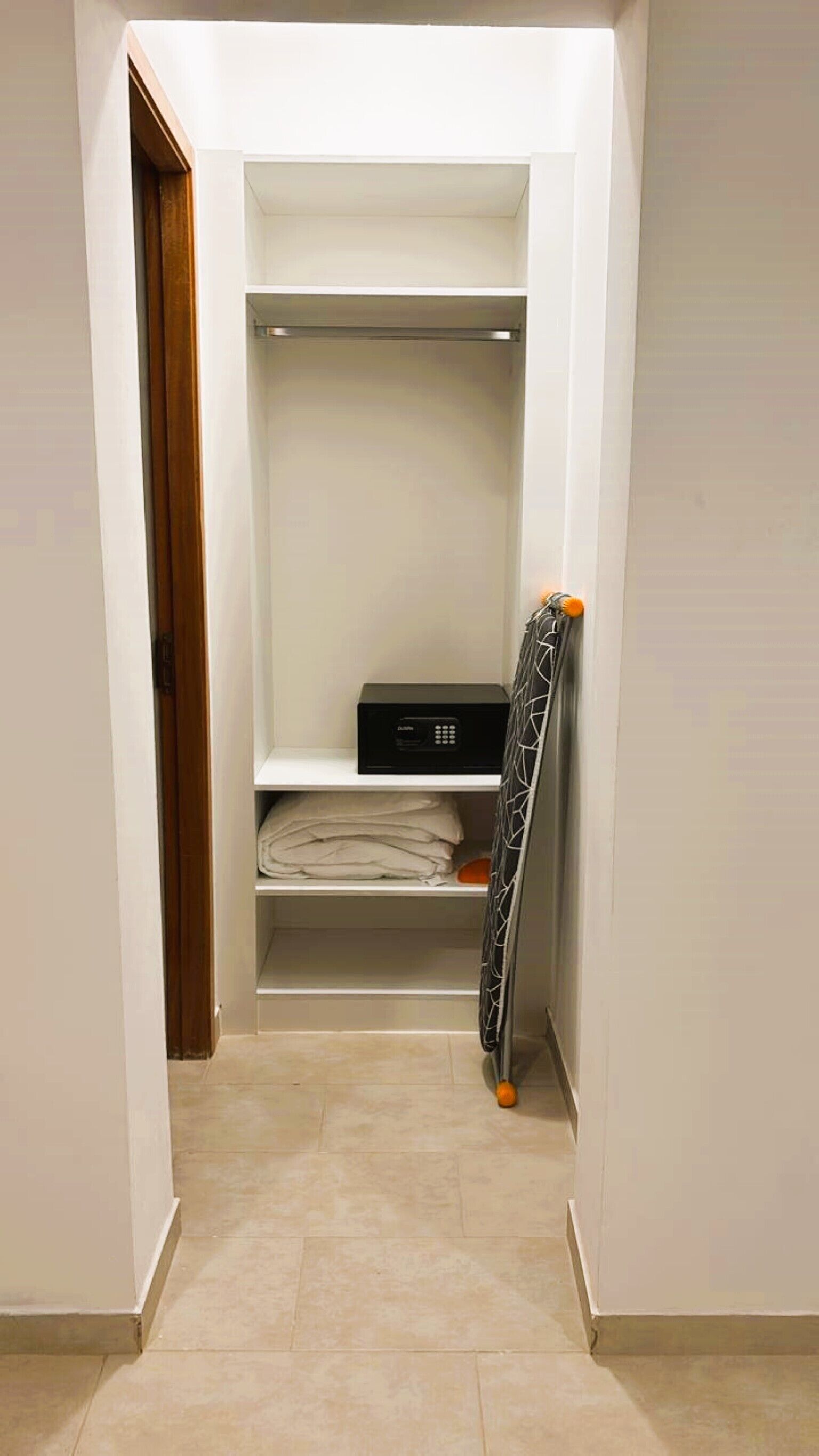 Un couloir étroit avec une armoire blanche contenant des vêtements pliés et un appareil électronique noir posé sur une étagère.