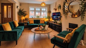 Een knusse woonkamer met groene banken, een salontafel en een televisie waarop Netflix wordt afgespeeld.