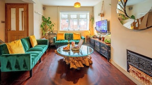 A cozy living room with a green sofa, a glass coffee table, and a TV on a wooden cabinet.