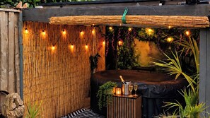 Un bain à remous avec un décor de bambous, entouré de plantes et illuminé de guirlandes lumineuses.