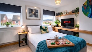 A modern bedroom with a bed, bedside table, lamp, and a TV displaying 'NETFLIX'.