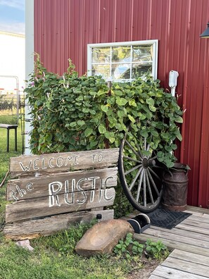 A rustic welcome sign with a wooden wagon wheel, a metal barrel, and a wooden bench.