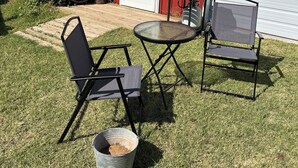 A red building with a white garage door, a wooden deck, a grill, two chairs, and a metal bucket.