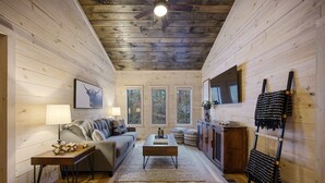 Interior acolhedor de uma cabana com piso de madeira, um sofá, uma mesa de centro, uma televisão e uma lareira.