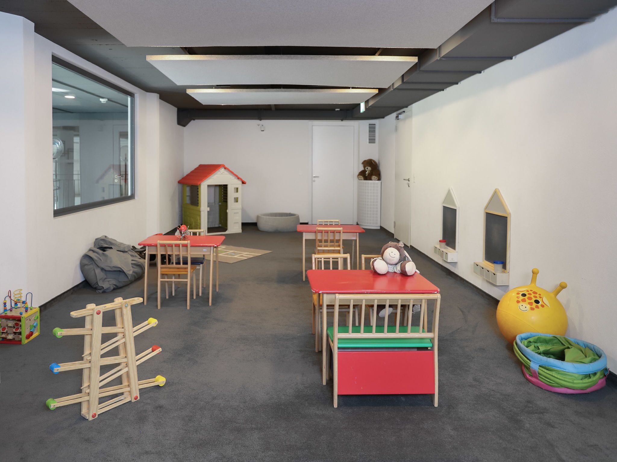 Una sala giochi per bambini con tavoli, sedie, una casetta e giocattoli.