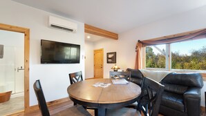 A modern living room with a round wooden table, black leather sofa, and a mounted flat-screen TV.