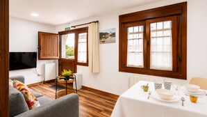 A room with a dining table set, a sofa, a TV, wooden flooring, and a window with curtains. - Brisas de Andrín - Near Andrín Beach, Llanes (Andrin)