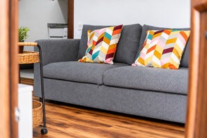 A grey sofa with colorful chevron-patterned pillows, a wicker side table, and a wooden floor. - Brisas de Andrín - Near Andrín Beach, Llanes (Andrin)