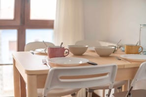 A dining table with plates, bowls, and a mug, set in a room with a window and white chairs. - Apartment in Llanes near the beach - El Refugio de Andrín (Andrin)