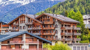 Un immeuble en bois à plusieurs étages, doté de balcons, qui se dresse sur un fond de paysage montagneux.