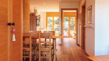 Un intérieur en bois comprenant un coin repas, une cuisine et une porte-fenêtre coulissante donnant sur une terrasse extérieure.