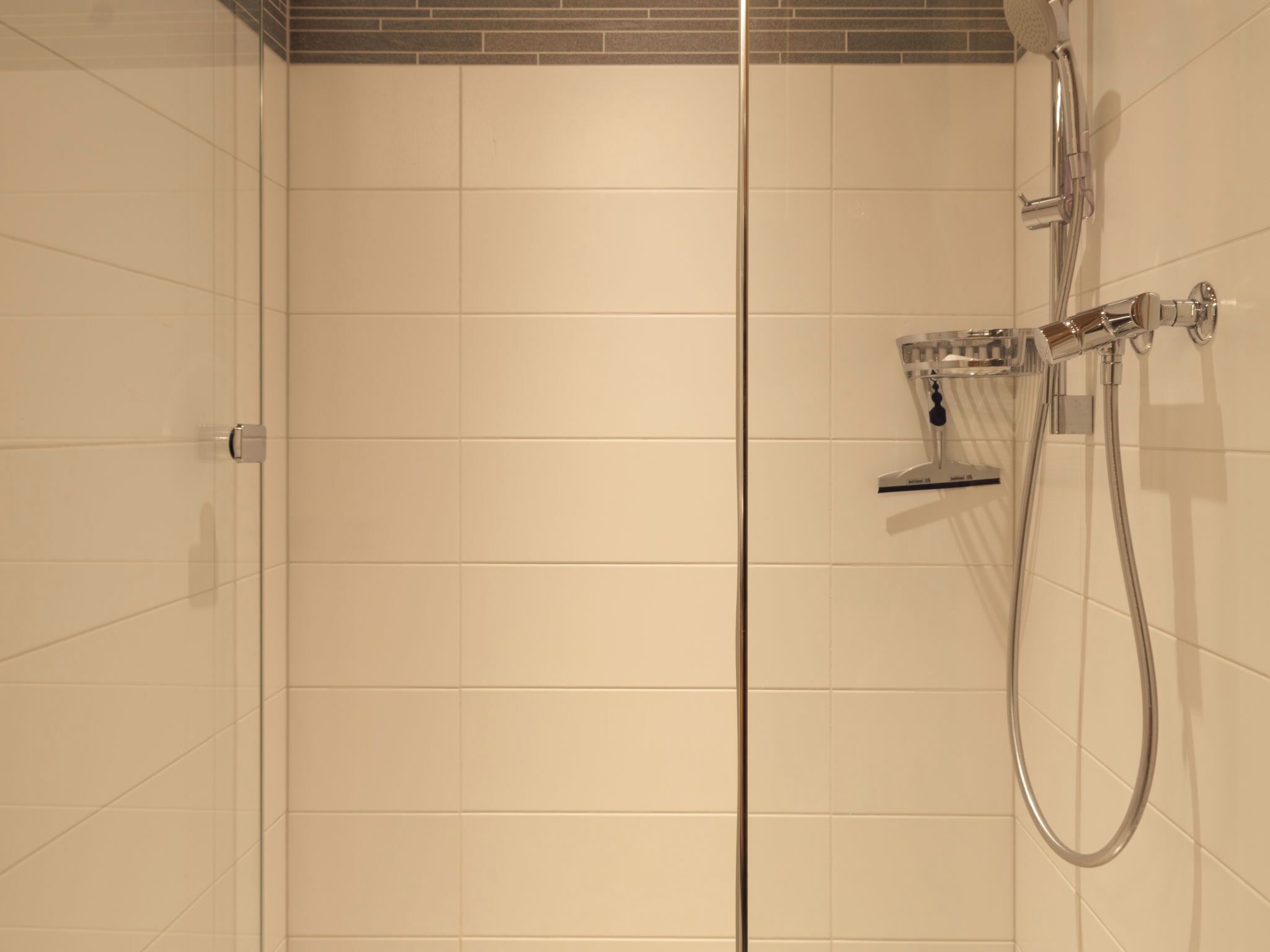 Un bagno moderno rivestito di piastrelle bianche, con cabina doccia in vetro e soffione cromato.