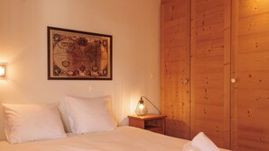 Un lit bien fait, avec du linge de lit blanc, une armoire en bois, une carte encadrée accrochée au mur et une lampe de chevet.