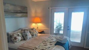 A hotel room with a bed, a nightstand, a lamp, a window, and a door. - Lakefront Retreat - 3BR/2BA Cherry Lake Home + Private Boat Dock (Madison)