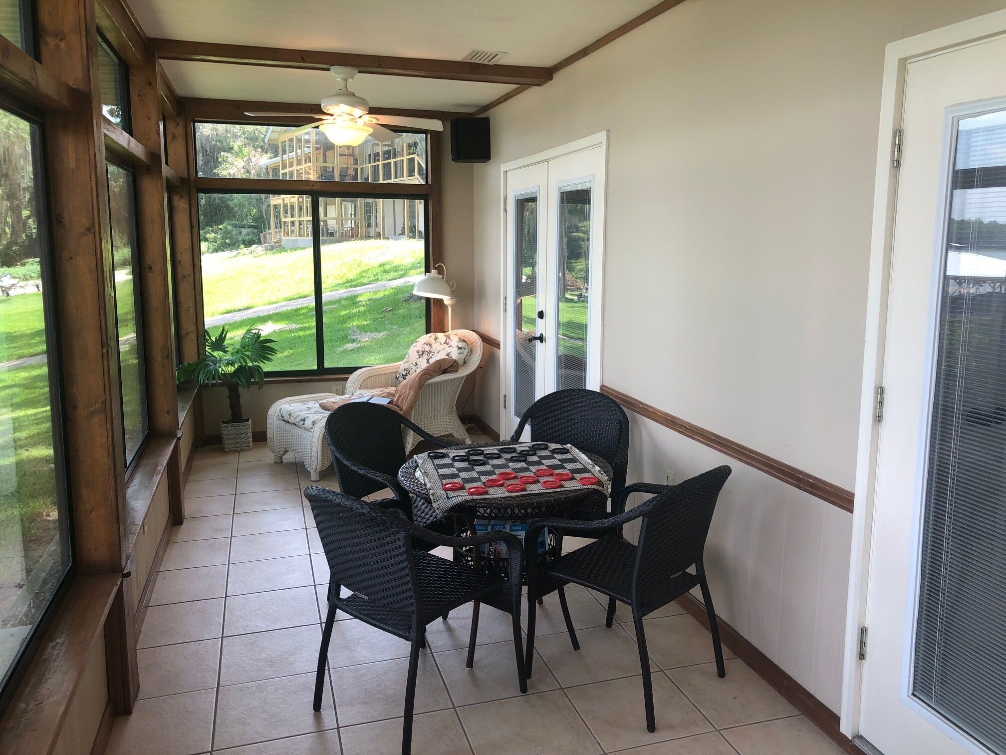 Una habitación soleada con vistas a un césped verde, un ventilador de techo, una mesa con mantel a cuadros y sillas de mimbre.