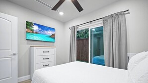 Une chambre à coucher avec un lit, un téléviseur fixé au mur, une porte-fenêtre coulissante et une porte en bois.
