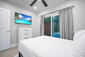 A bedroom with a bed, a TV mounted on the wall, a sliding glass door, and a wooden door.