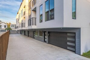 A modern multi-story residential building with a row of garage doors, a wooden fence, and a clear sky.