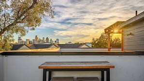 Une terrasse sur le toit, avec une table et deux chaises, d’où l’on peut admirer le panorama de la ville au coucher du soleil.
