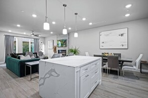 A modern kitchen with a marble island, pendant lighting, and a dining area with a view of greenery.