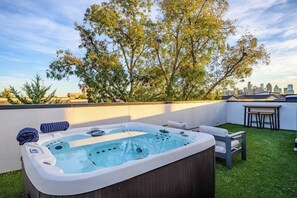 A rooftop patio with a hot tub, outdoor seating, and a view of a city skyline.