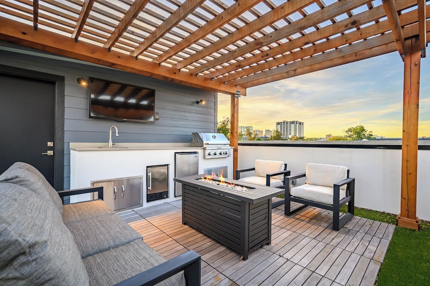 Un patio al aire libre con una parrilla, asientos, un televisor y vistas del horizonte de la ciudad.