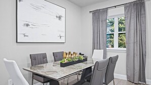 Une salle à manger moderne avec une table en marbre, des chaises recouvertes d’un tissu gris, une pièce maîtresse noire et un grand tableau abstrait accroché au mur.